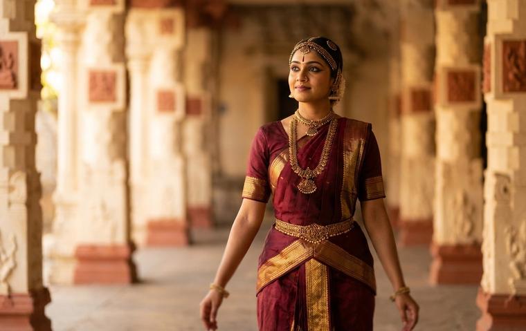 Bharatanatyam dancer in maroon and gold costume expressing a rasa through her eyes and face in warm temple lighting