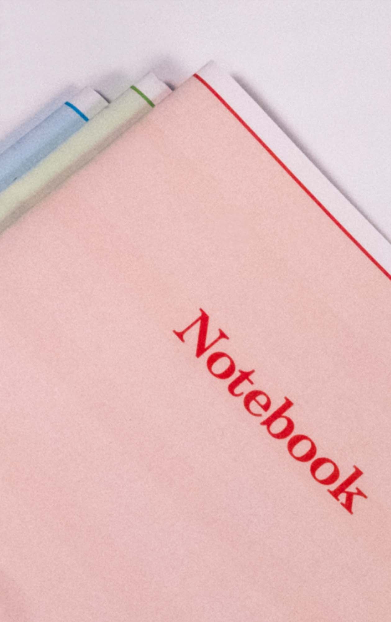 Pastel notebooks with blue, green, and red edging and Notebook printed on the pink cover.