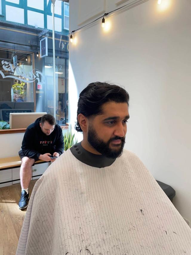 Slicked-back cut and full beard shape-up, the arcade window behind