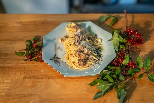 Finished pasta plated on a wooden counter with botanical details.
