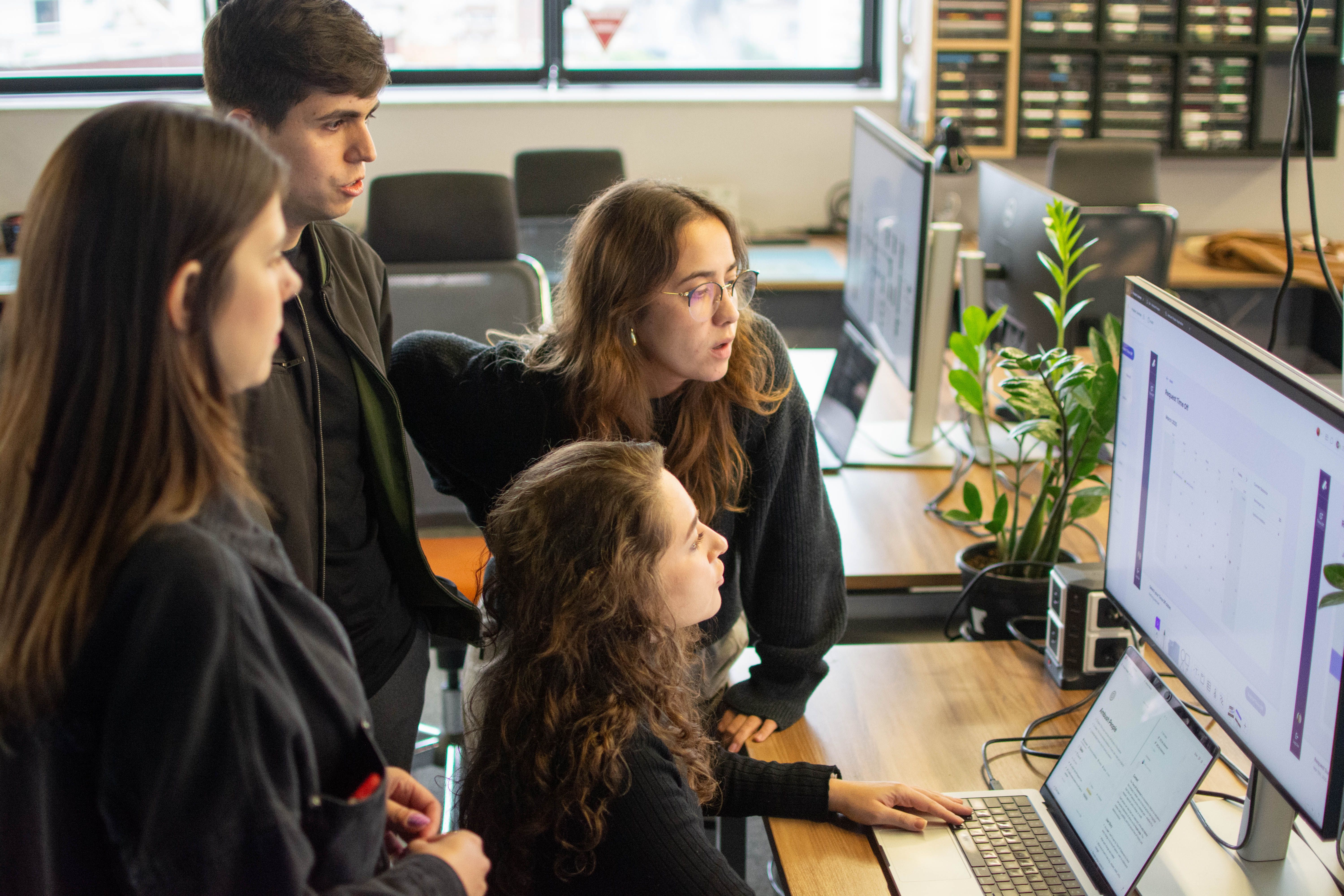 Four colleagues collaborating around computer monitors in modern office