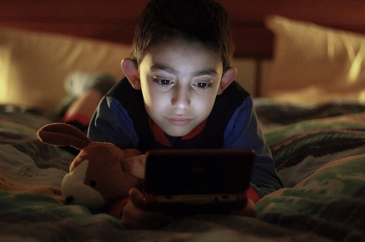 Young boy playing video games in bed