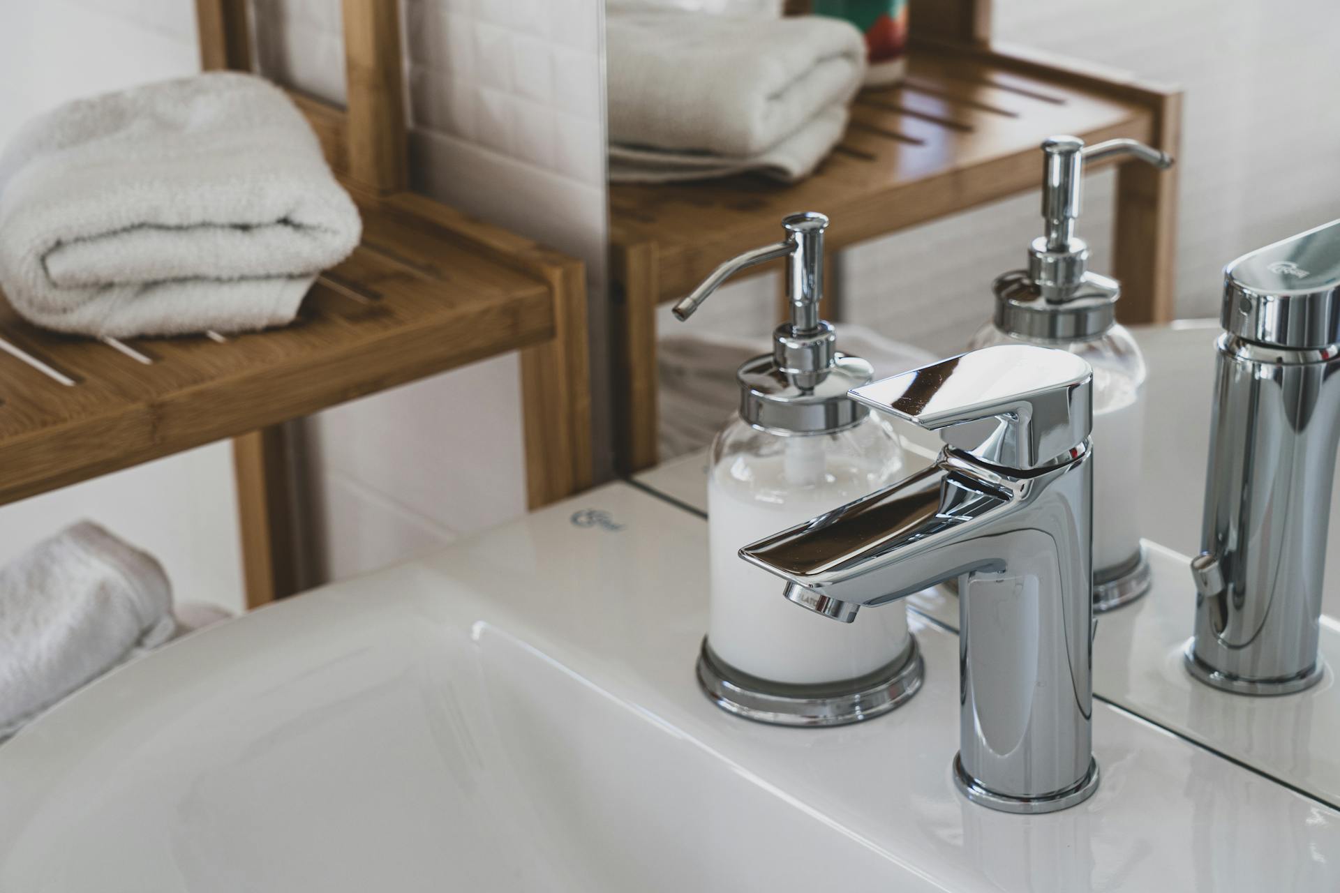 Primo piano di un rubinetto cromato lucido per bagno accanto a dispenser di sapone in vetro