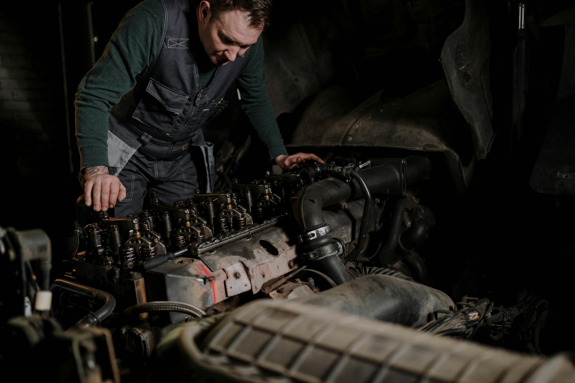Mécanicien penché sur un moteur diesel poids lourd dans une baie d'atelier, culasse exposée