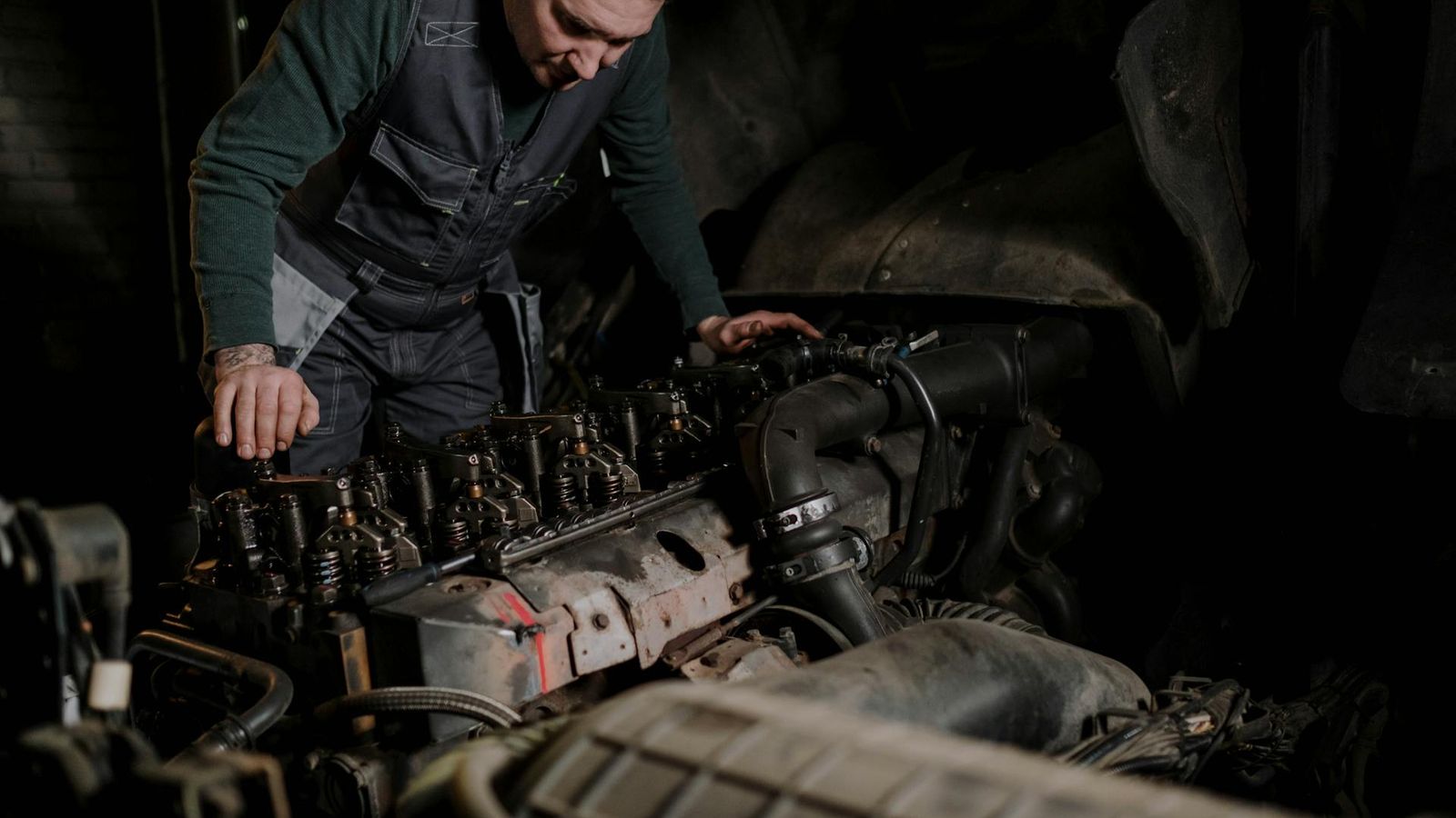 Meccanico chinato su un motore diesel pesante in un'officina con la testata cilindro esposta