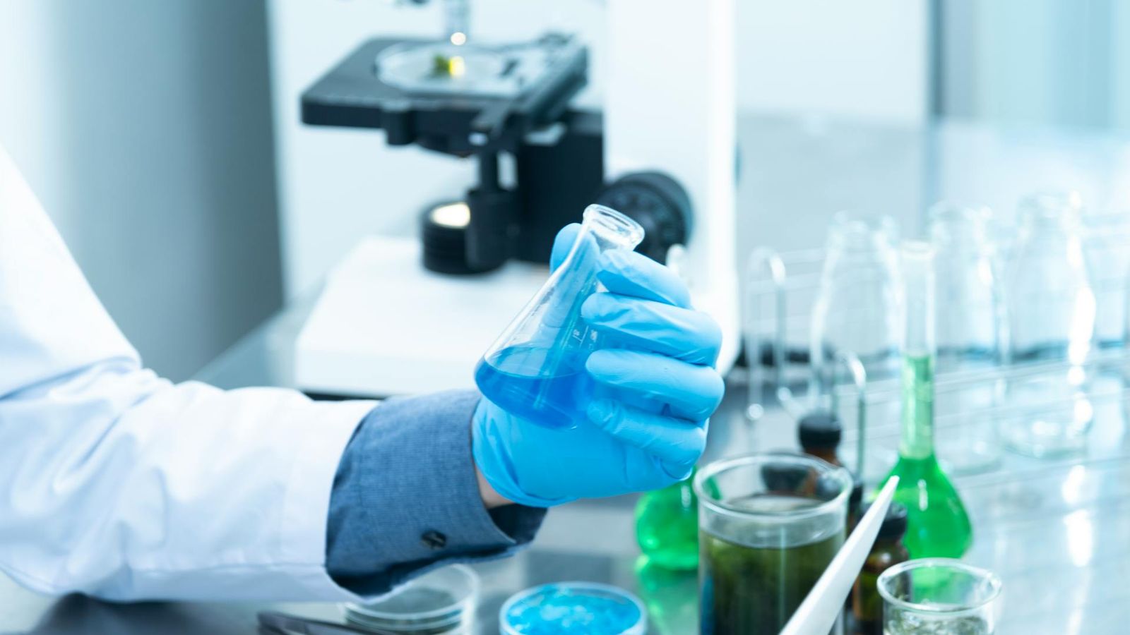 Behandschuhte Hand prüft eine klare Glasflasche unter kontrollierter Beleuchtung