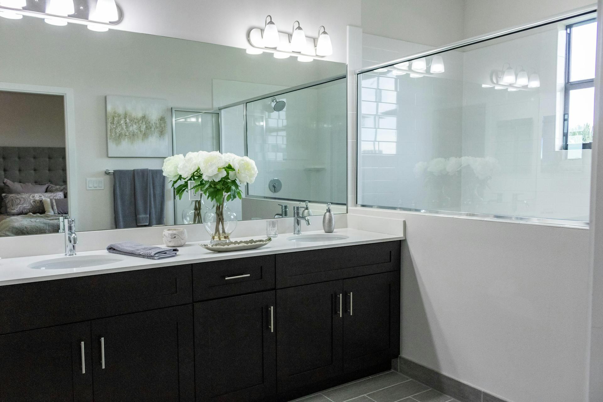 Bagno moderno con doppia vanità, mobiletti scuri, grande specchio e top in quarzo bianco