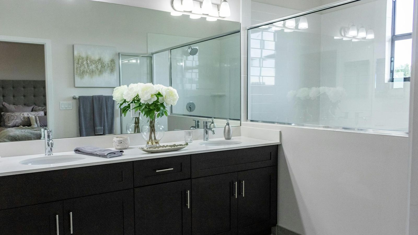 Salle de bains moderne à double vasque avec meubles foncés, grand miroir et plan en quartz blanc
