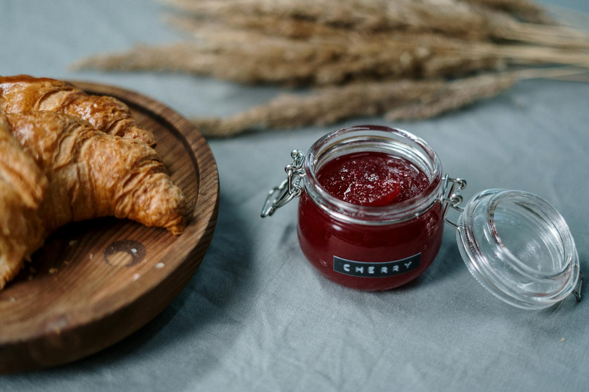 Confiture de cerise dans un petit pot en verre à côté d'un croissant frais sur une planche en bois