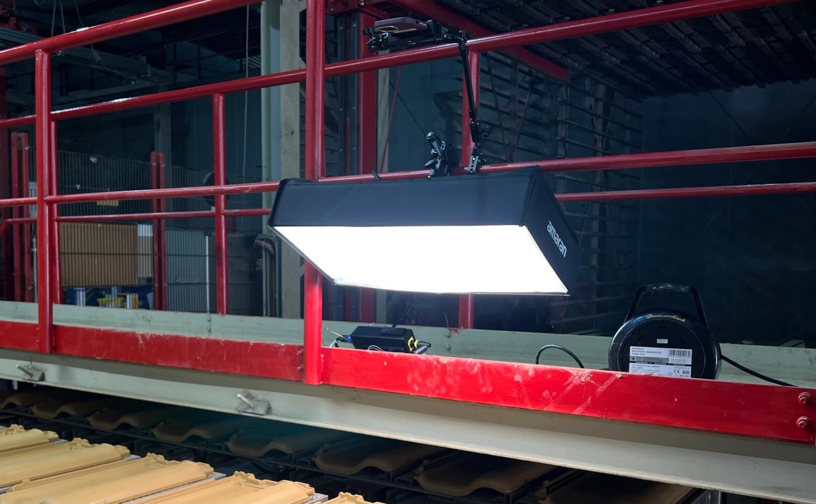 An Amaran flood light is mounted on rails in a manufacturing plant with an iPhone mounted on top to scan products for defects with AI-based machine vision software
