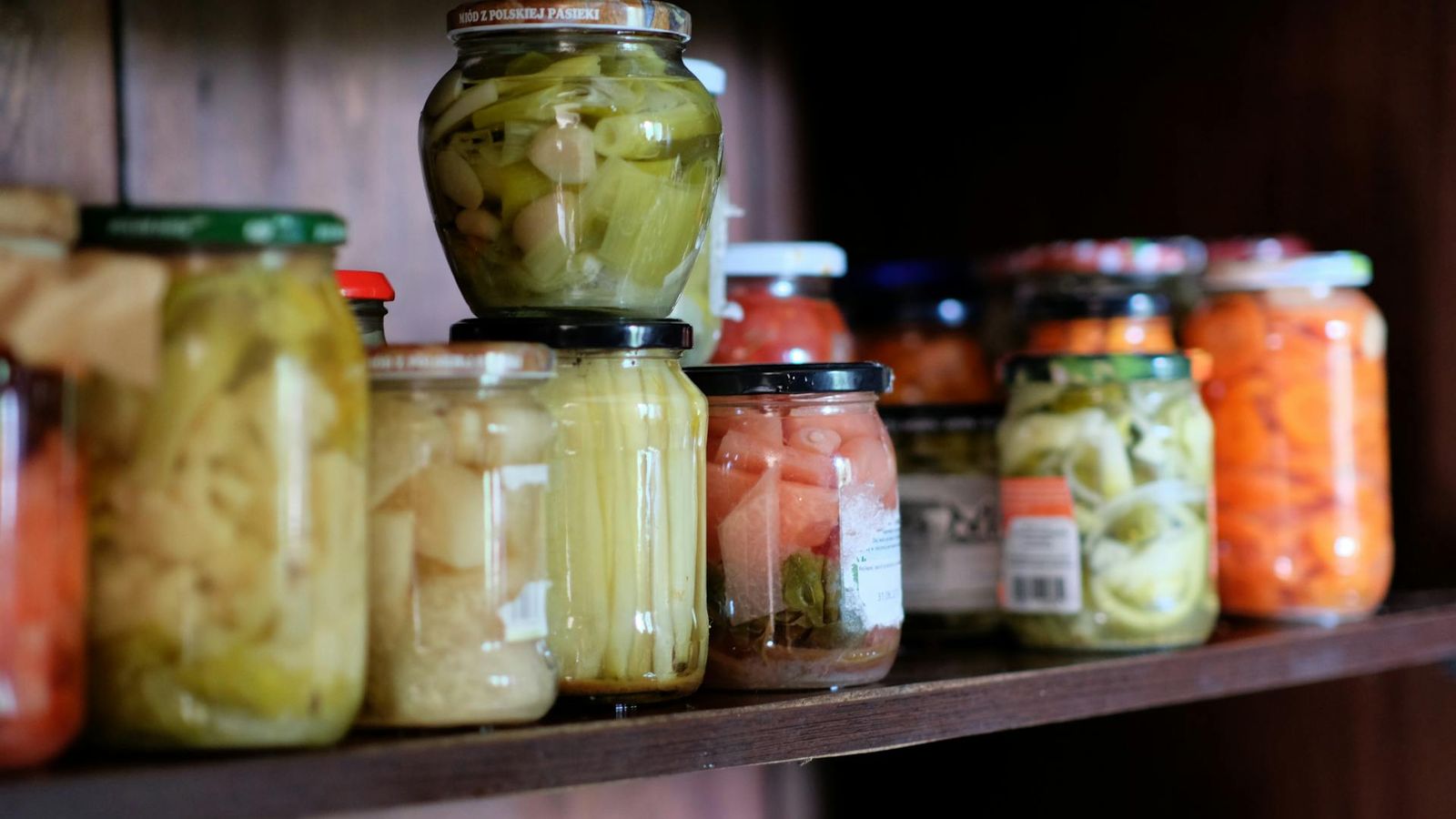 Prateleira de despensa em madeira alinhada com legumes e pickles em conserva caseira em frascos de vidro