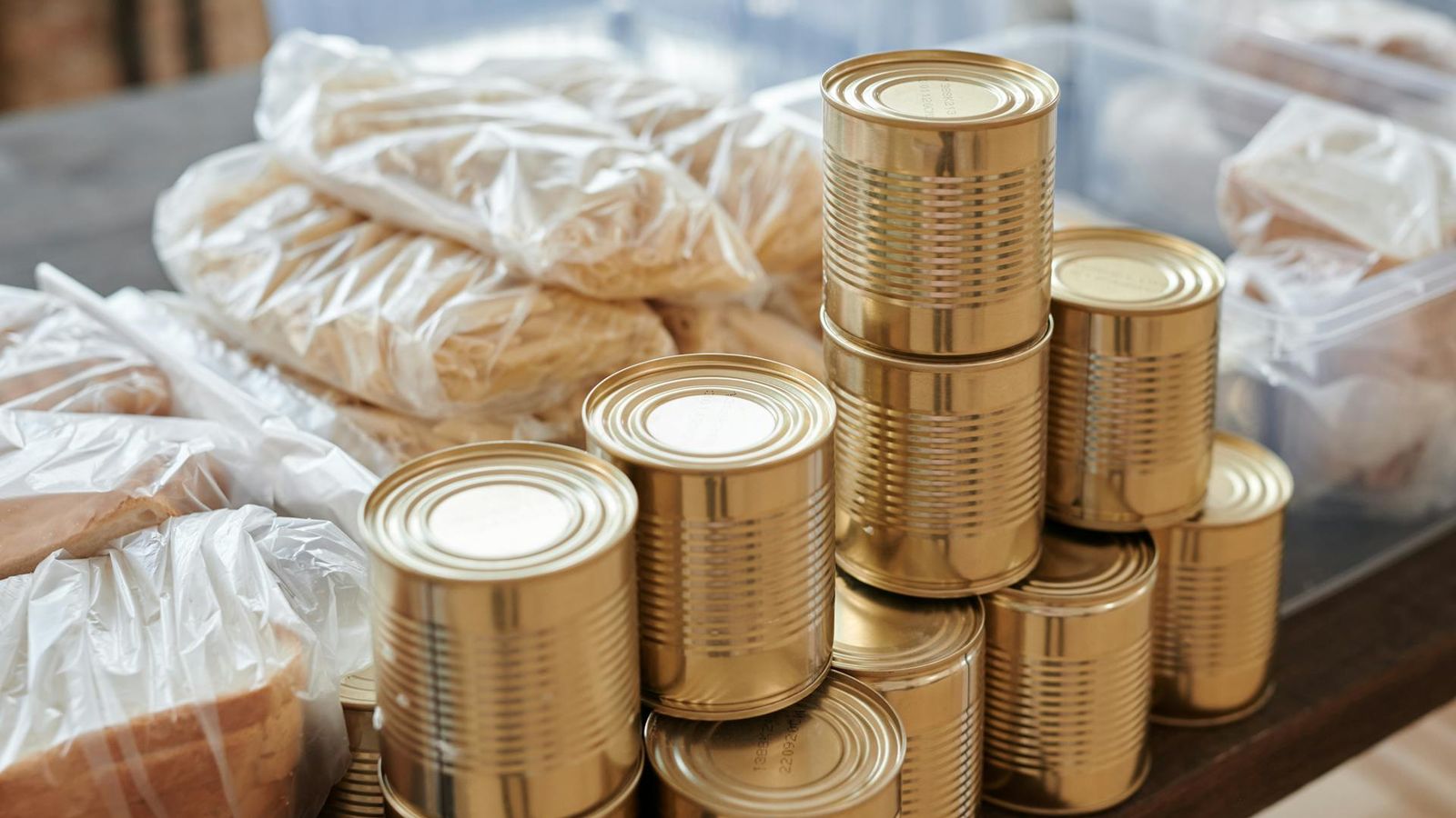Latas empilhadas ao lado de pacotes de pão embalados em plástico numa mesa de embalamento