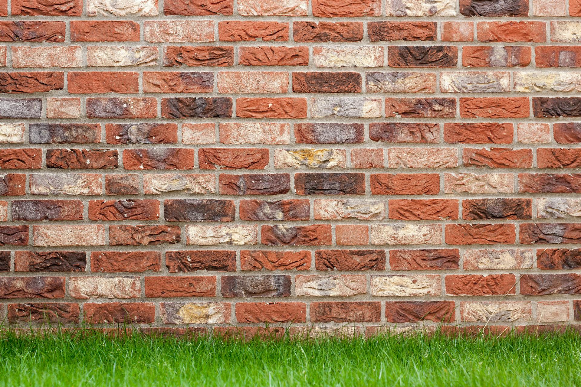 Primer plano de un muro de ladrillo rojo y amarillo con colores moteados y hierba en la base