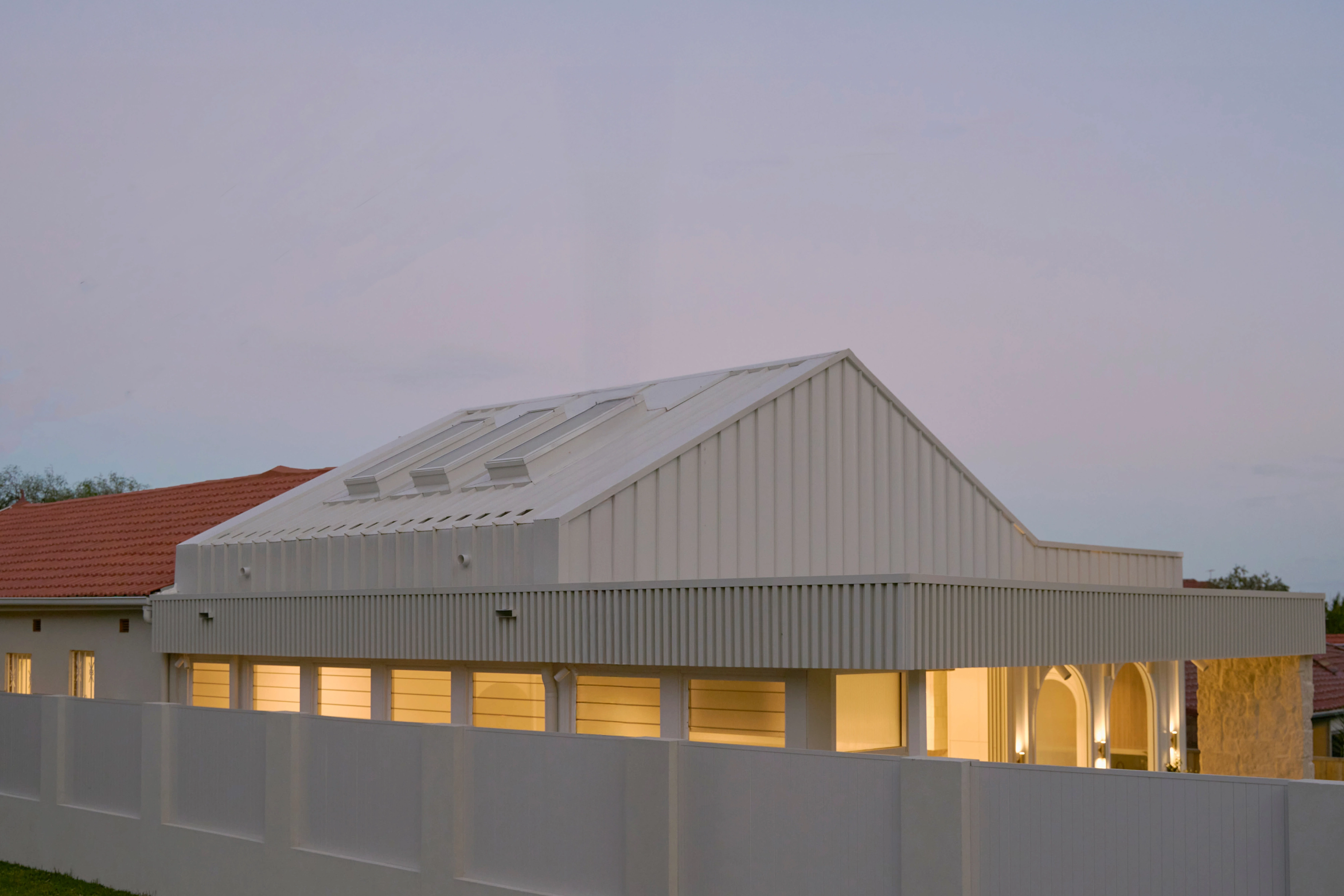 CONWAY rear extension at dusk with a gabled roof, skylights and illuminated arched openings.