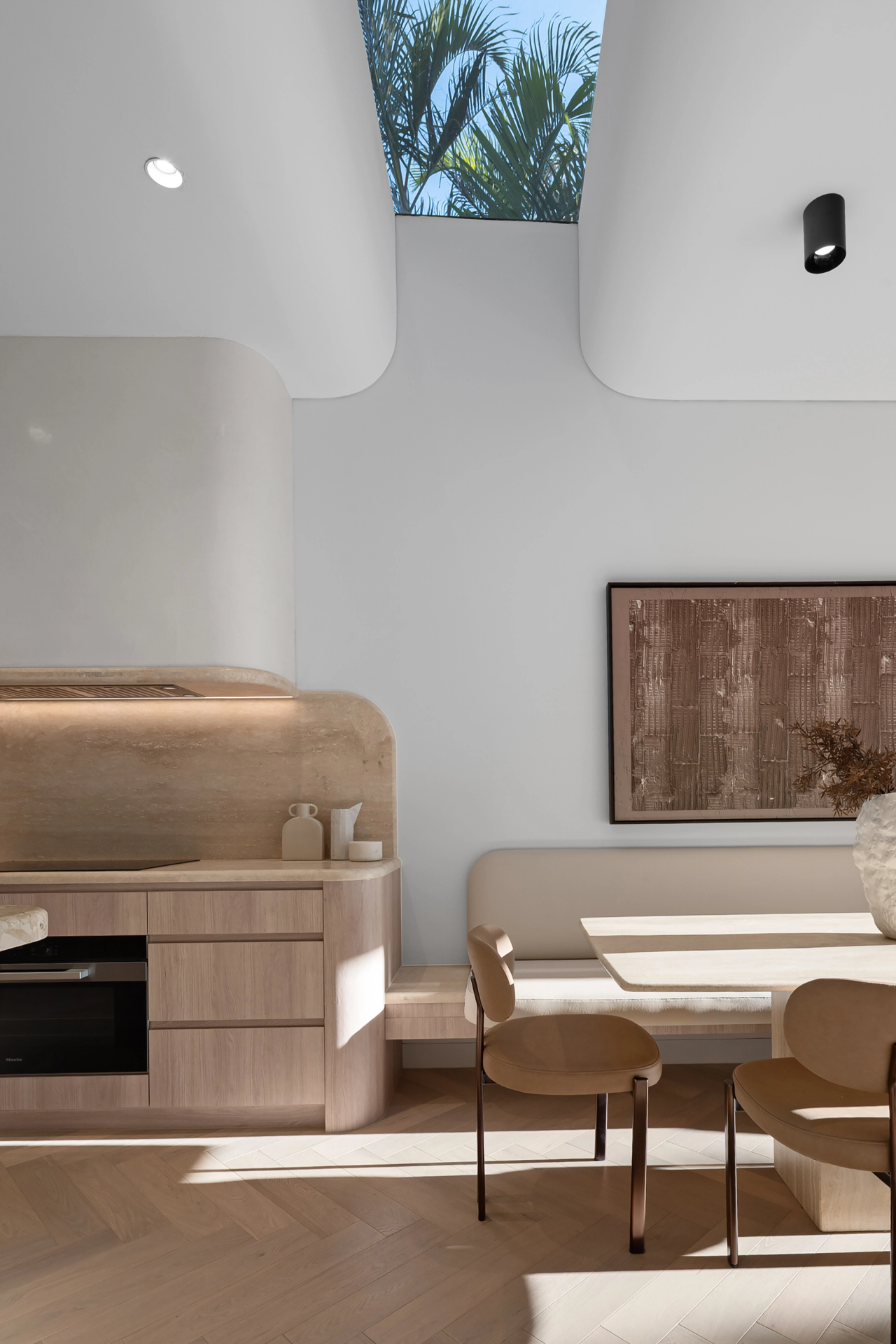 Dining nook beneath a curved skylight with timber cabinetry and a rounded stone splashback