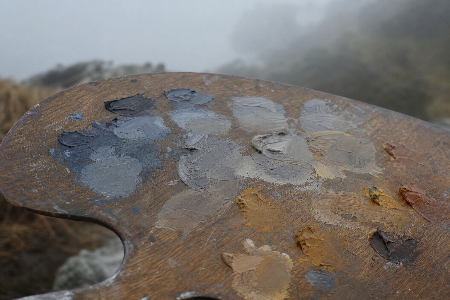 A wooden paint palette with cool and warm grey mixes and a limited set of earth colours