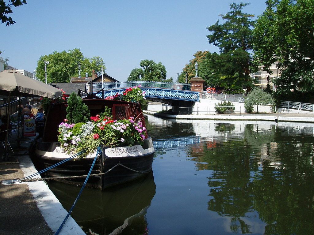 Narrowboat moored on a canal in Little Venice with buildings reflected in the water.