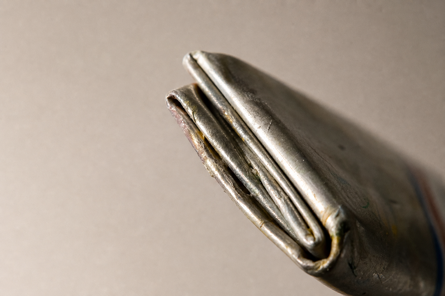 Close-up of a rolled and crimped metal paint tube end against a neutral background