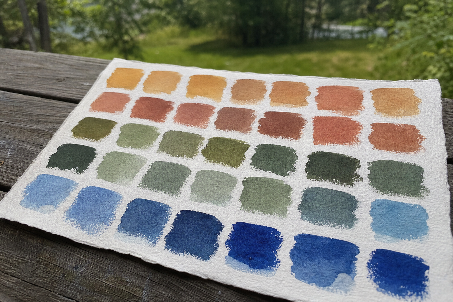 Rows of matte gouache colour swatches painted onto textured watercolour paper in natural daylight