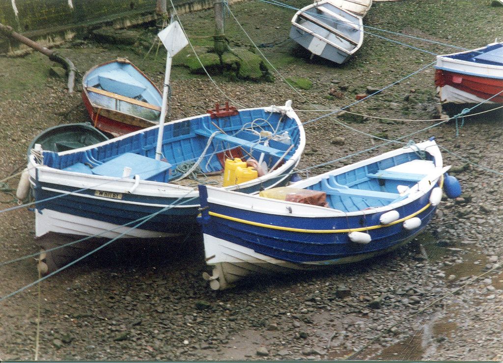 Small fishing boats moored in a narrow harbour beside coastal cottages