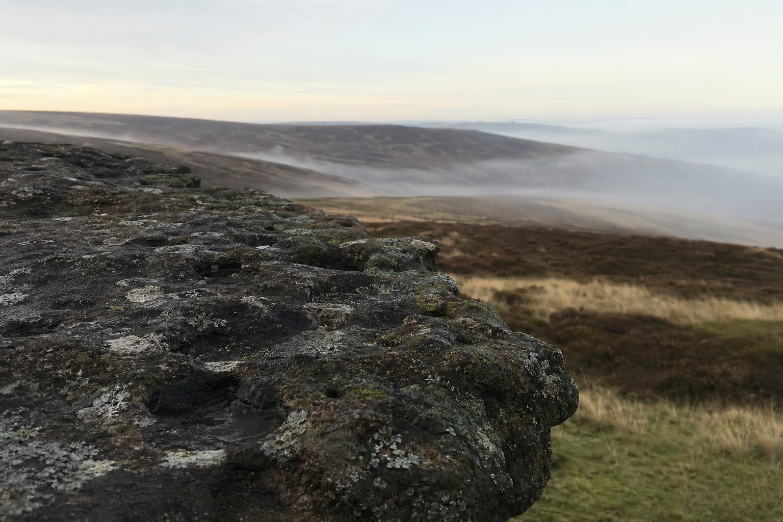 Gritstone rock edge above open moorland under a pale dawn sky