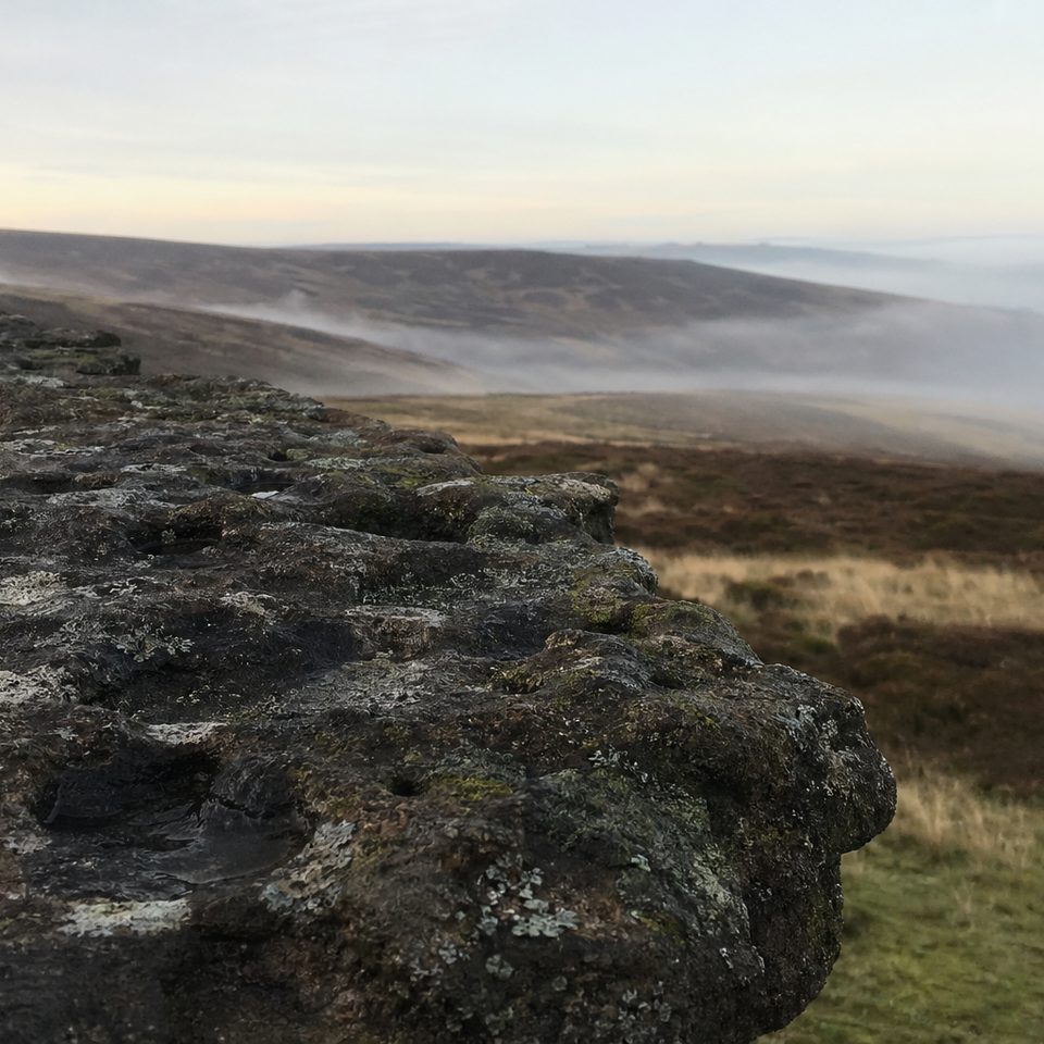 Gritstone rock edge above open moorland under a pale dawn sky
