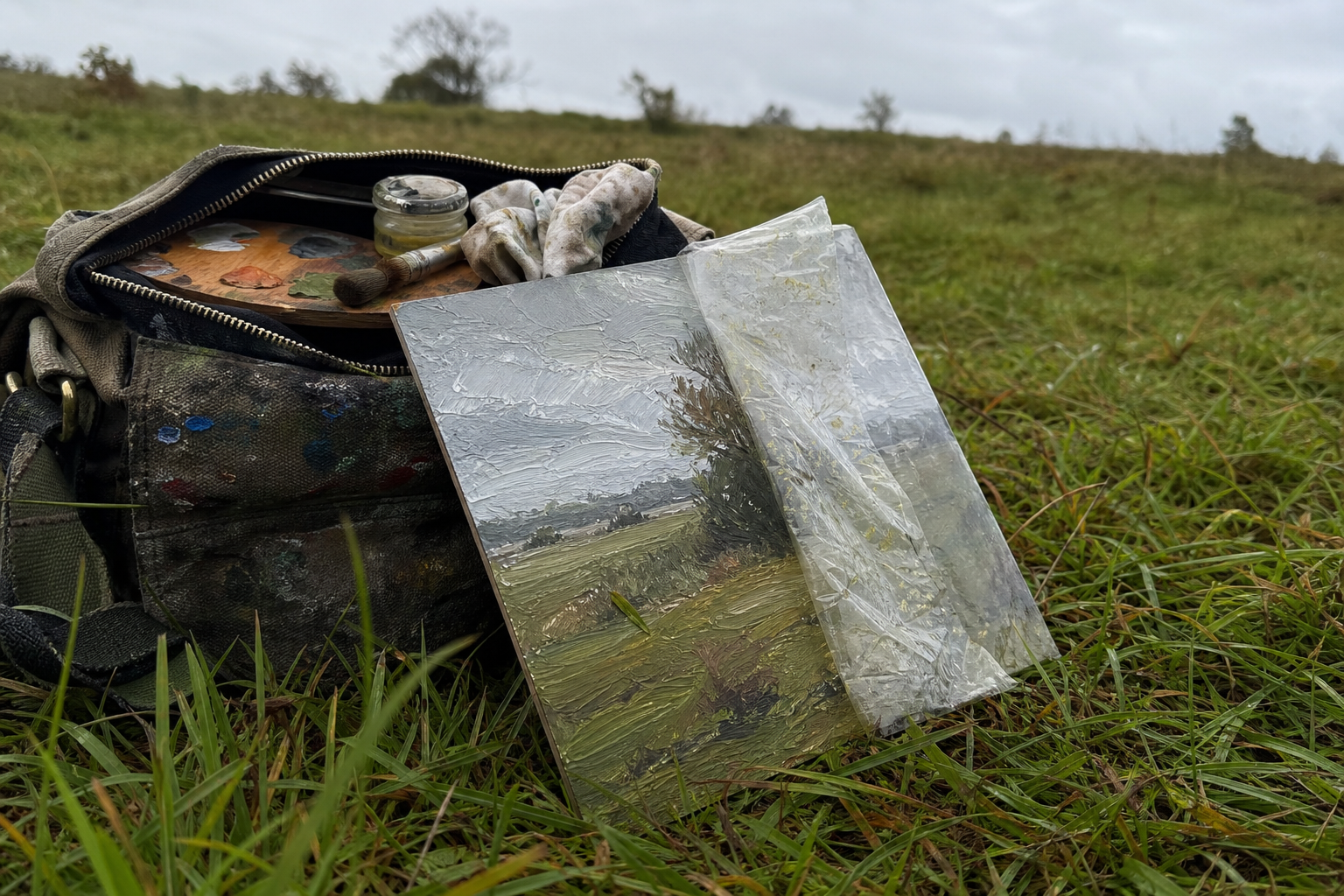 Freshly painted oil panel resting against a field bag in overcast outdoor light