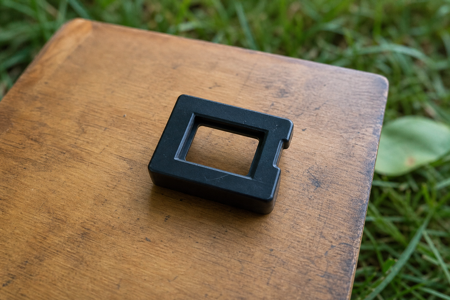 Small rectangular plastic artist viewfinder resting on a wooden sketchbook outdoors