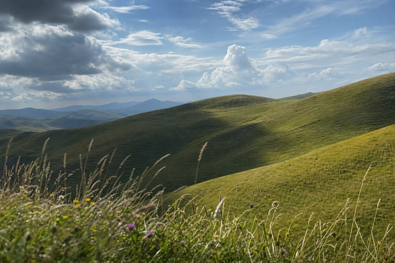 Dark cloud shadow passing over green rolling hills beneath a partly cloudy sky