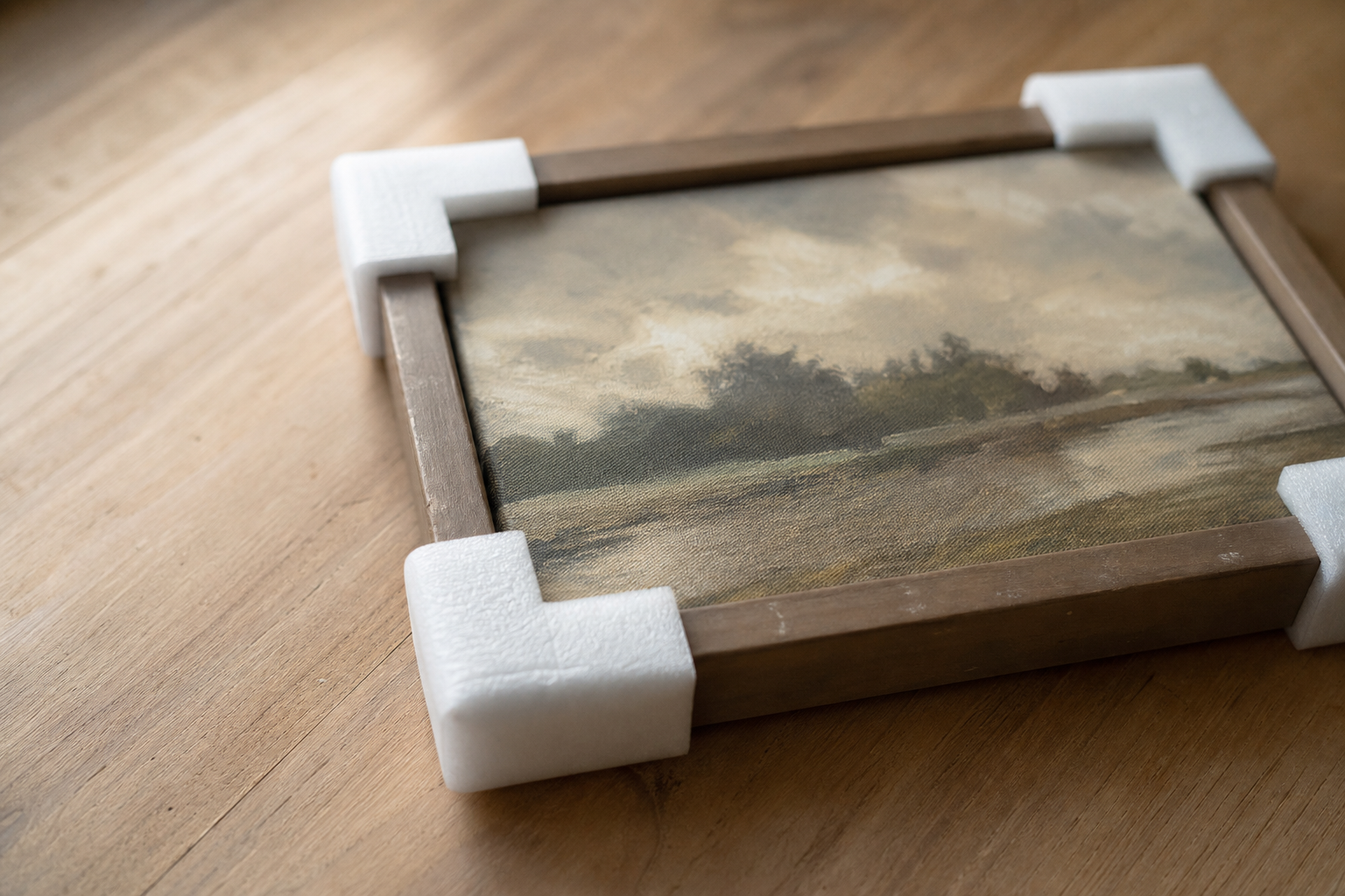 Foam corner protectors fitted to the corners of a small framed painting on a flat surface.