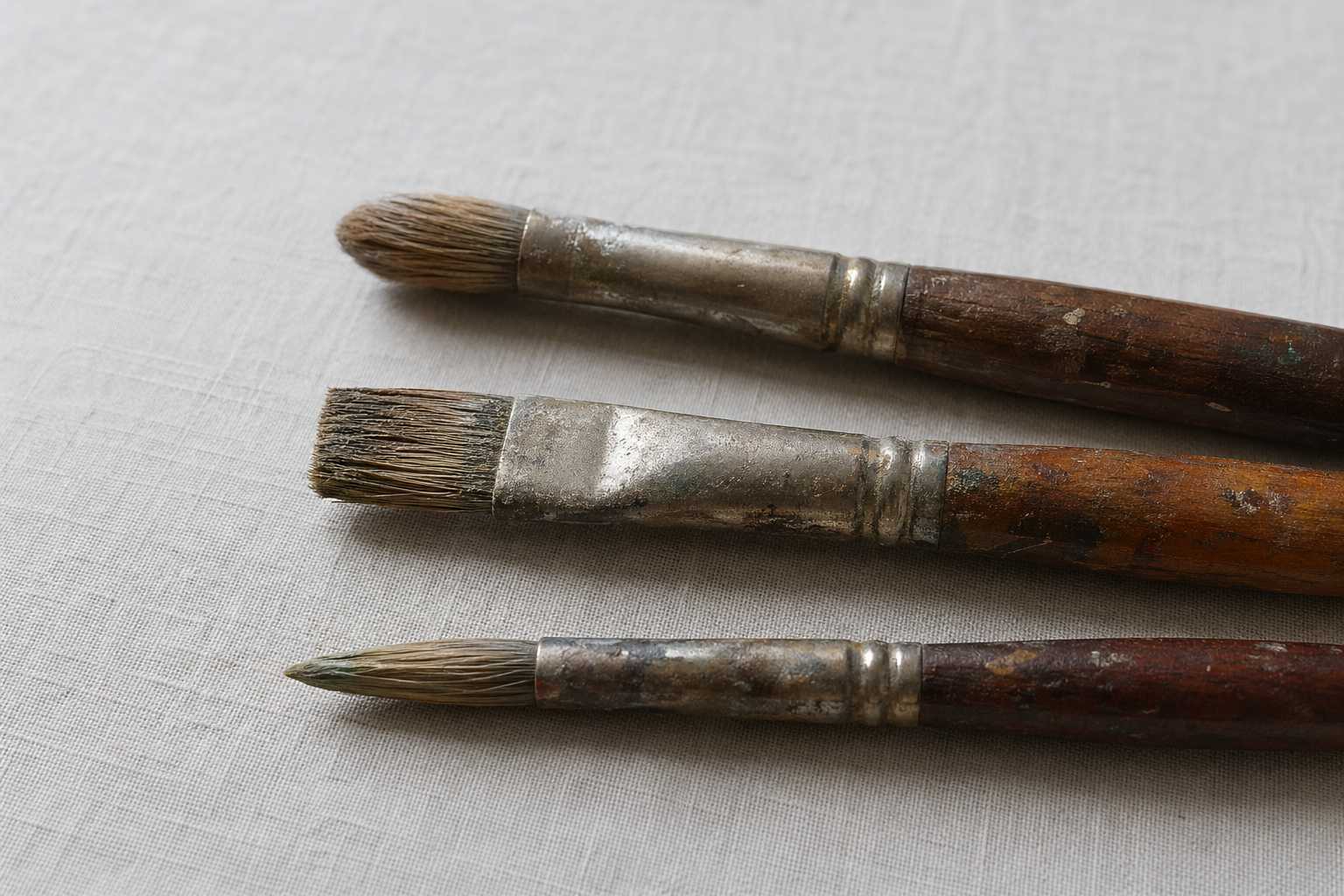 Three oil painting brushes showing filbert, flat, and round shapes against a neutral surface