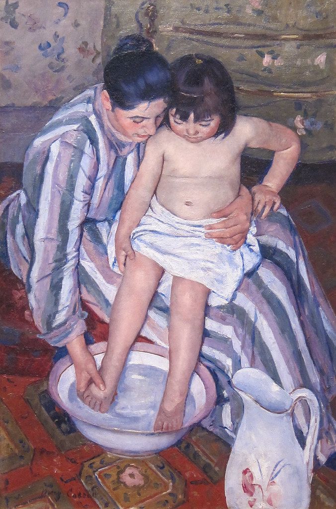 Woman leaning over a small child who sits in a basin during a bath, in a late 19th-century painting.