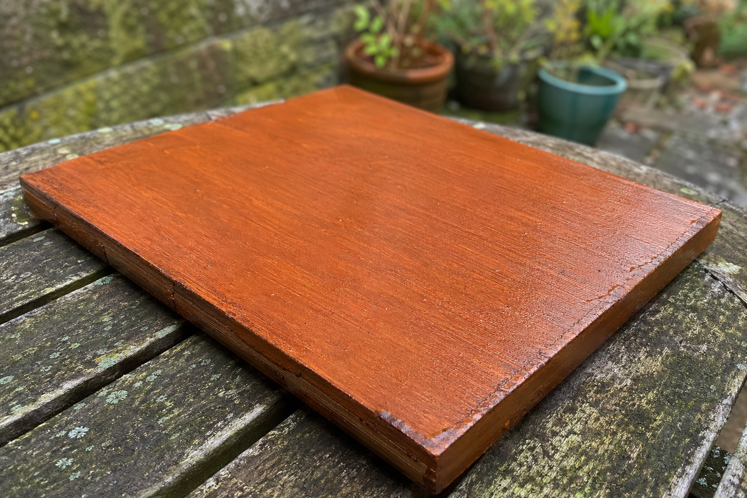 Small wooden panel coated in warm reddish-brown paint wash, drying in open air