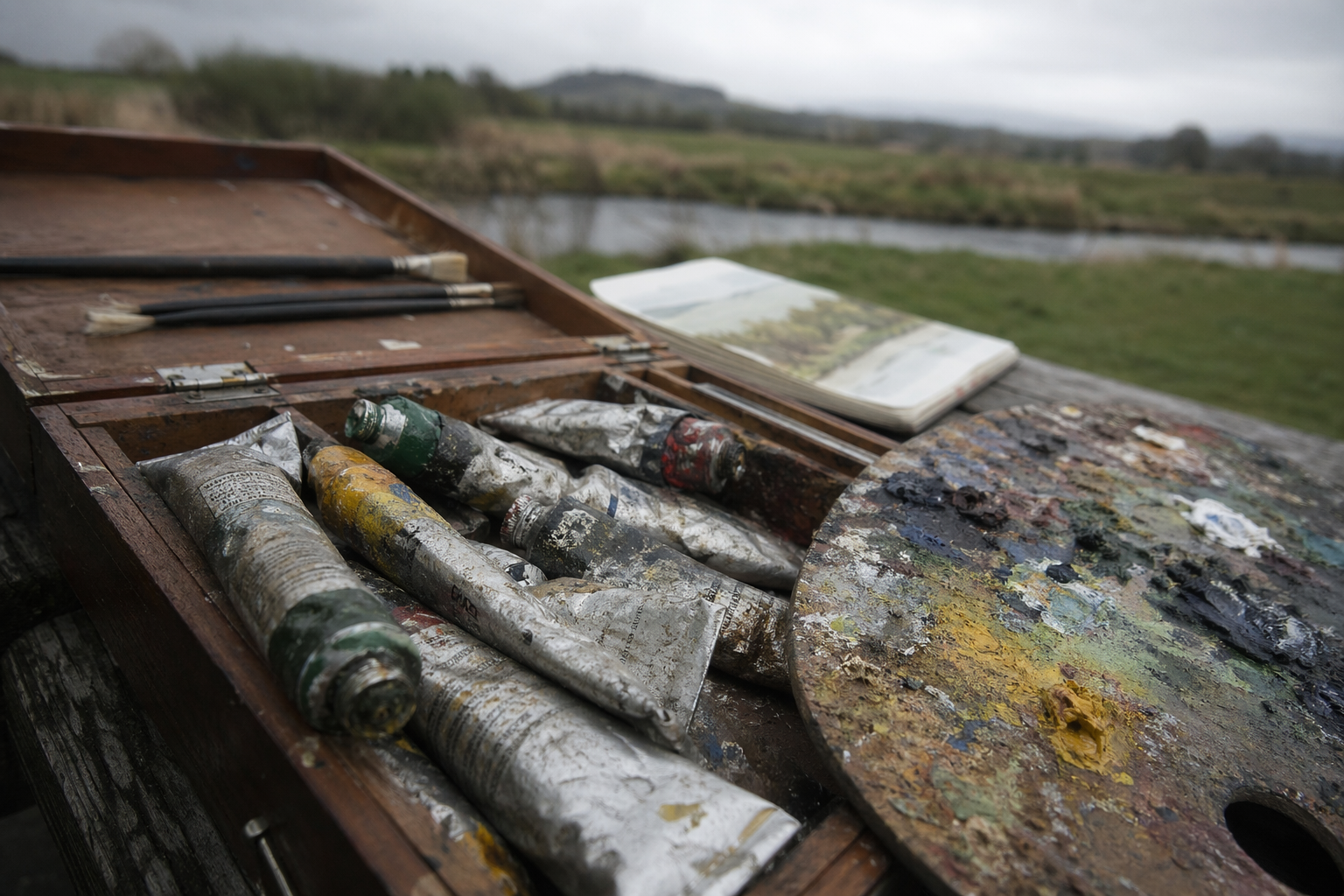 Several oil paint tubes arranged on an open wooden palette box outside