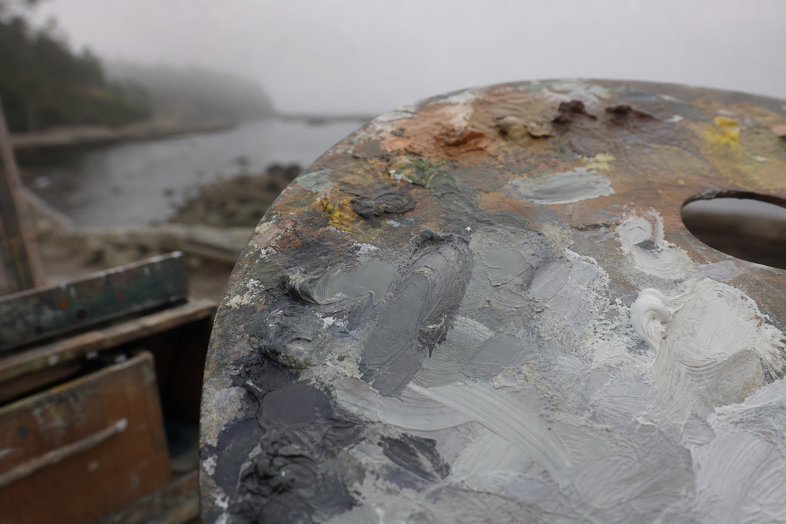 Close-up of an oil painting palette with cool grey fog tones mixed alongside muted earths