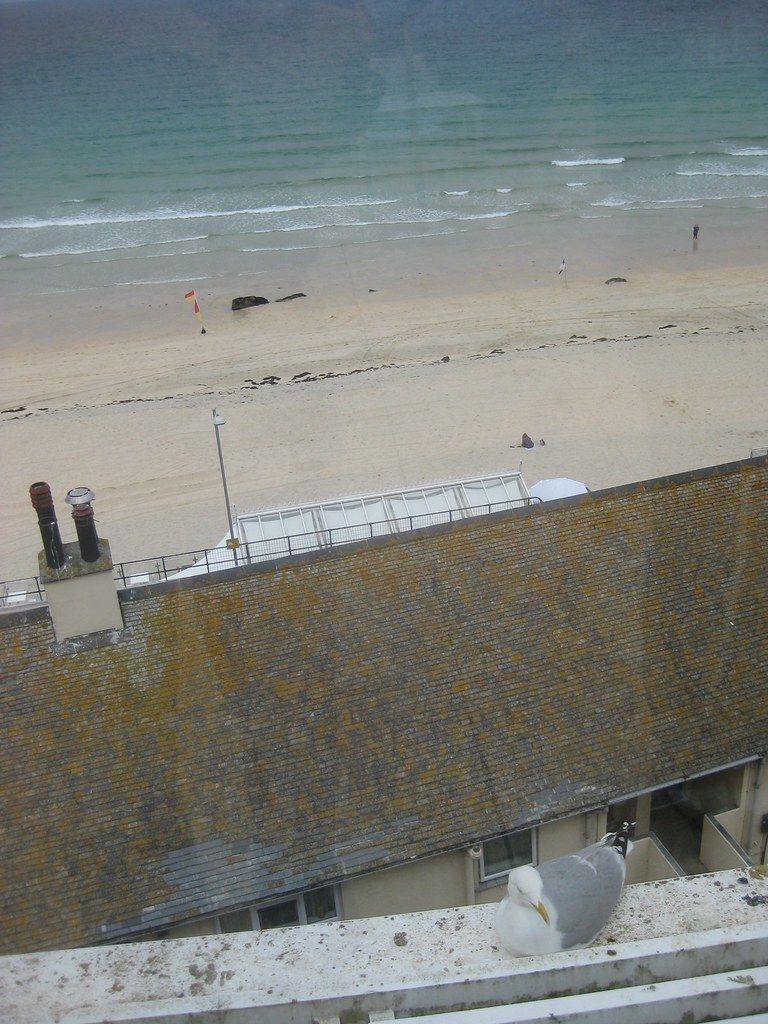 Coastal view from a cafe overlooking a beach, ocean, and nearby buildings in St Ives, Cornwall.