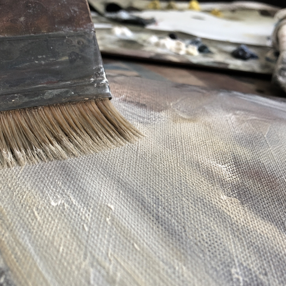 Stiff hog bristle brush dragging pale paint across textured canvas surface