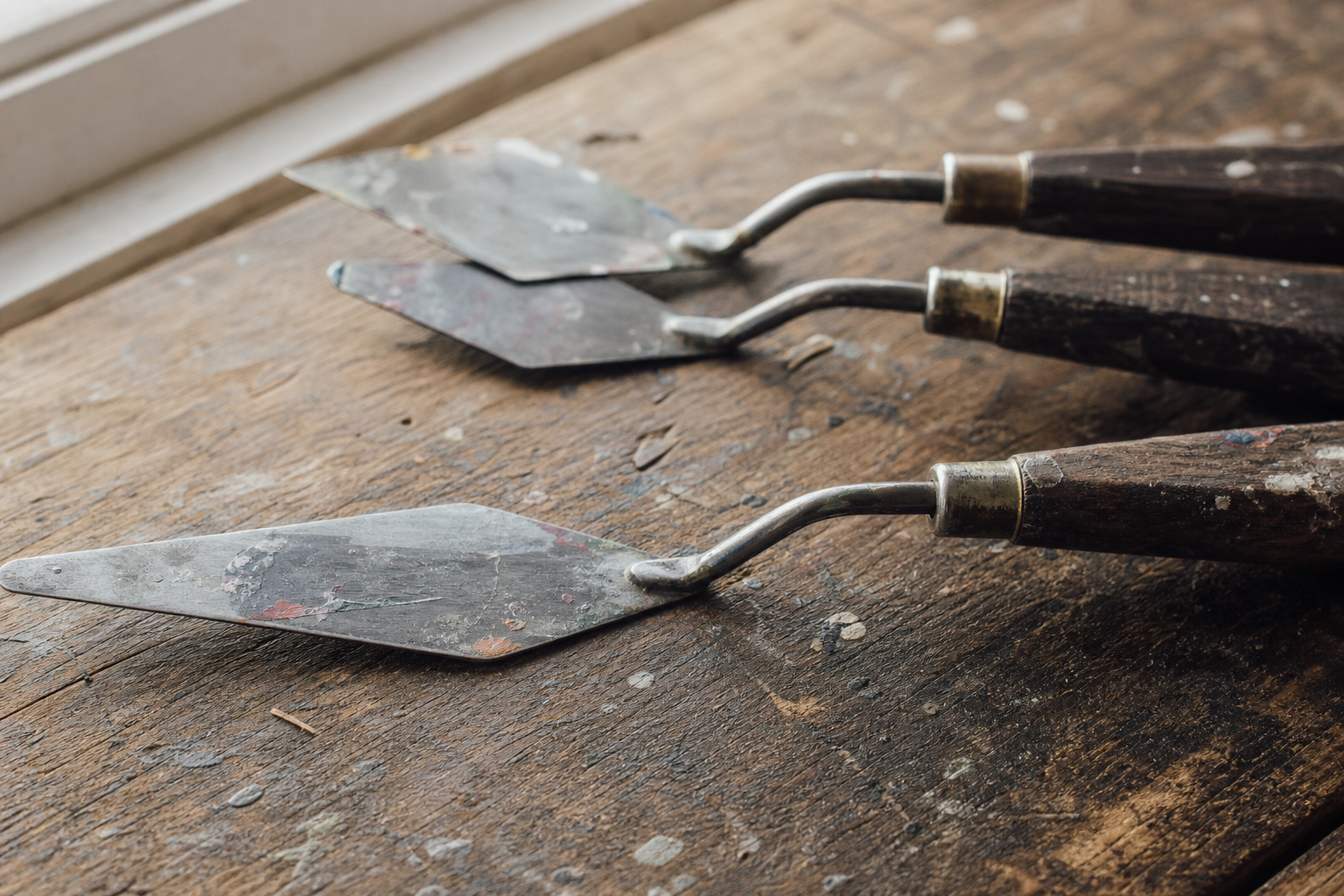 Close-up of three offset crank painting knives with wooden handles on a wooden surface