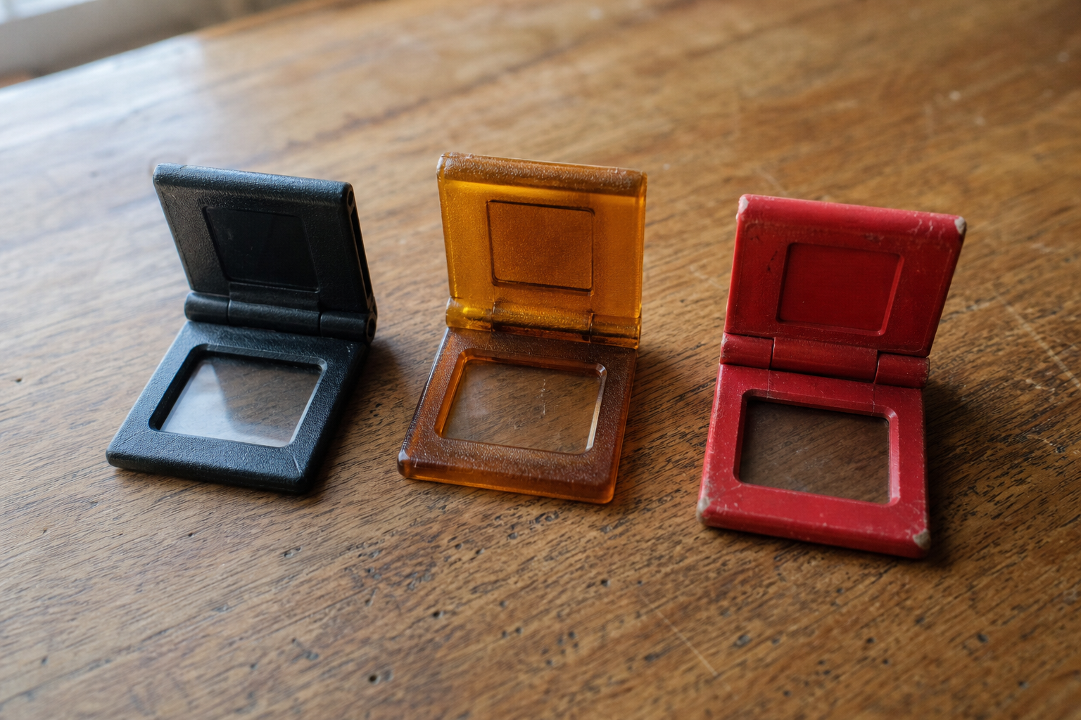 Three small plastic artist viewfinders laid flat on a wooden surface side by side