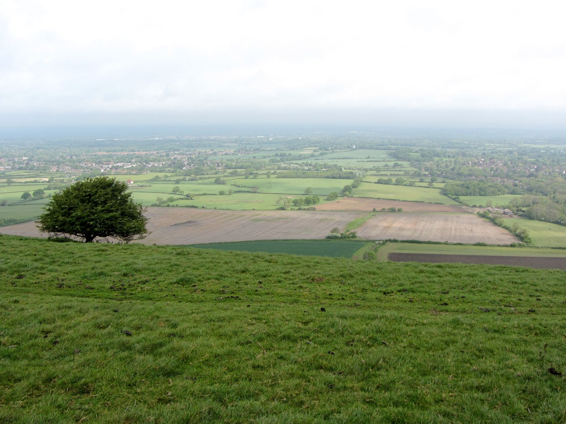 Landscape viewed north from Ditchling Beacon showing open fields and a distant horizon under a cloudy sky.