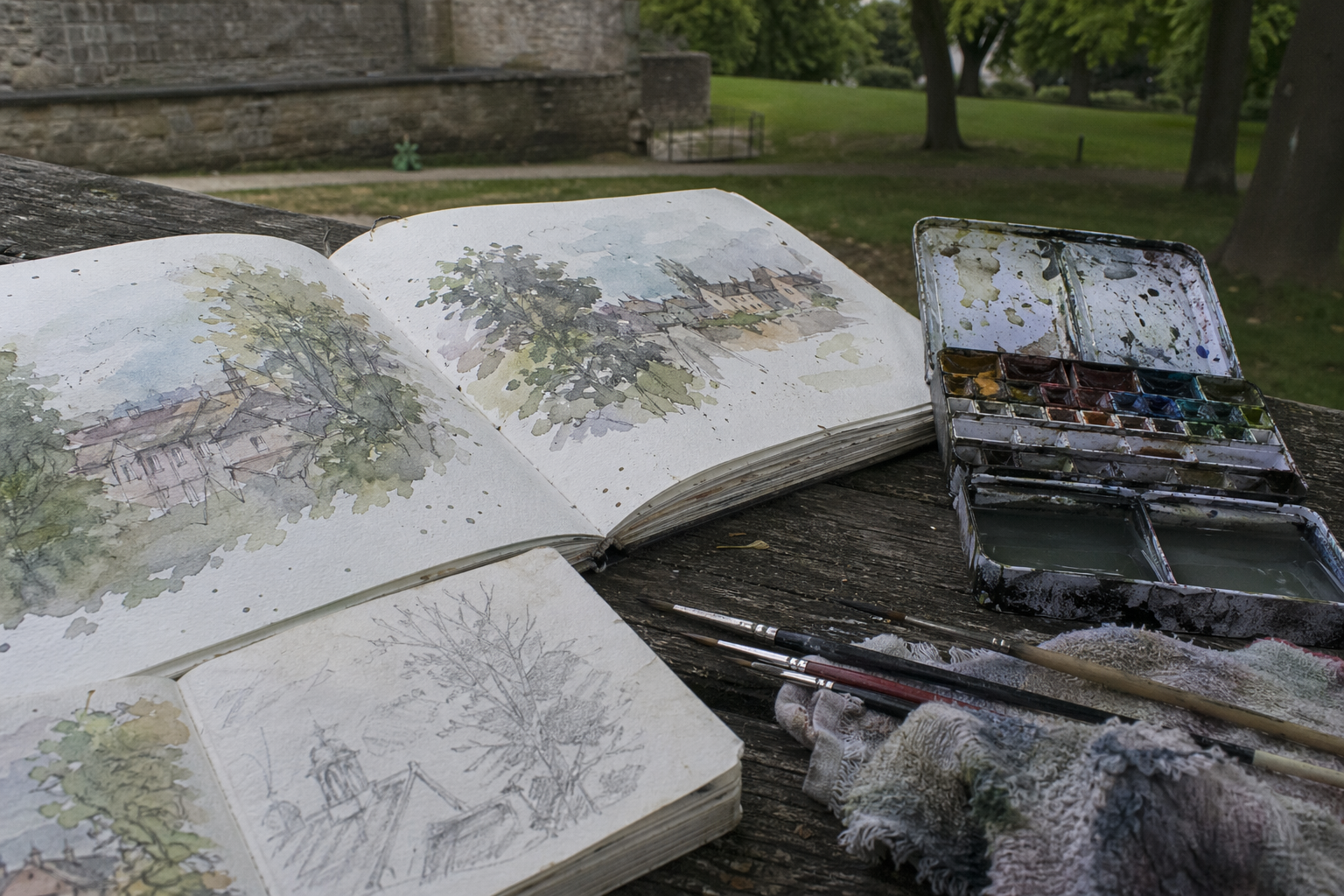 Open sketchbooks and a watercolour palette resting on a wooden outdoor table