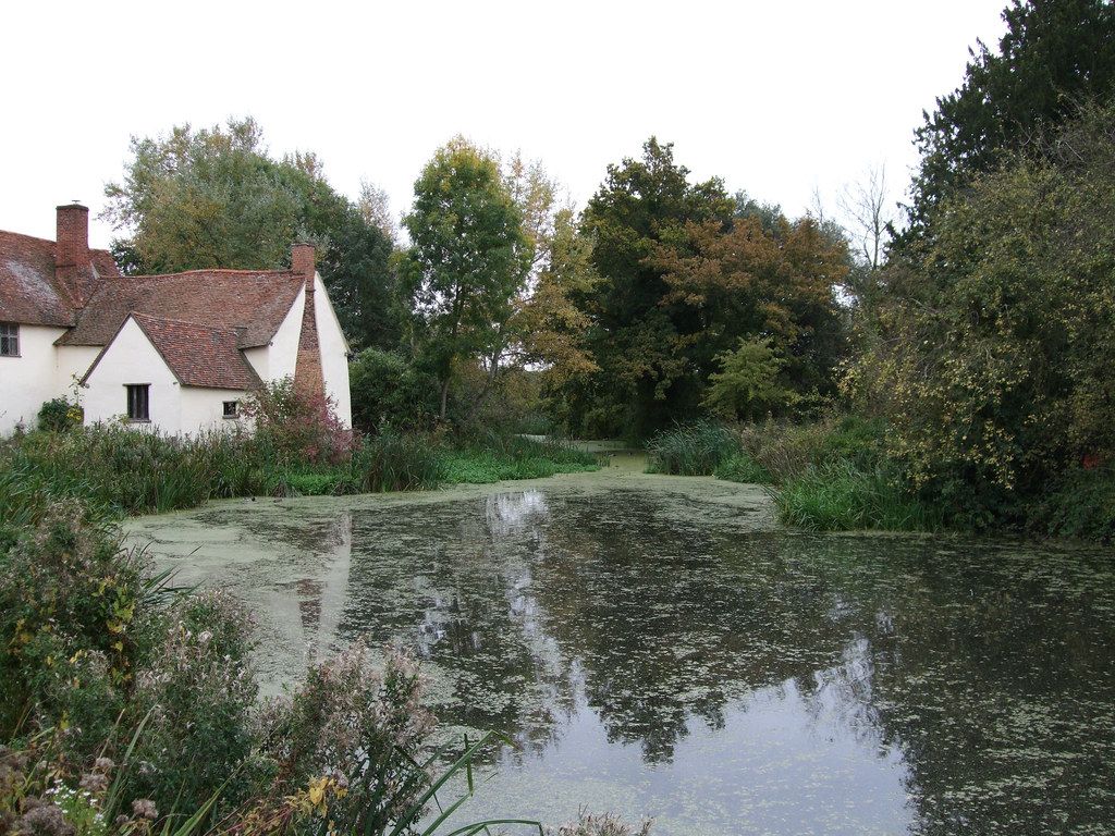 Riverside mill buildings and a cottage at Flatford Mill alongside a calm stretch of the River Stour in Suffolk.