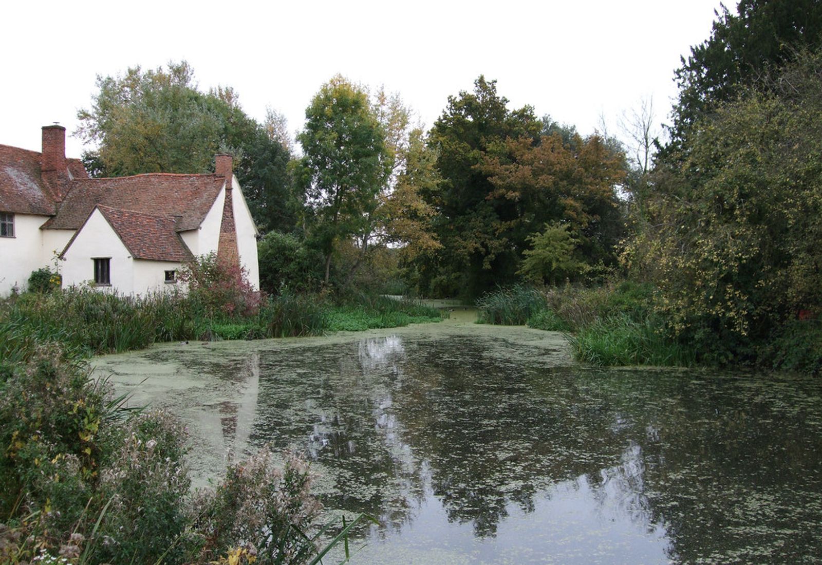 Riverside mill buildings and a cottage at Flatford Mill alongside a calm stretch of the River Stour in Suffolk.