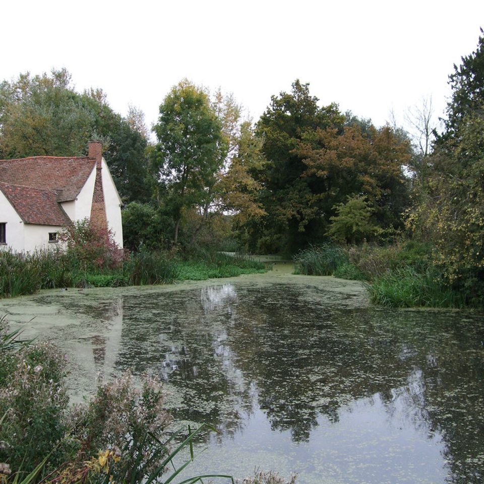 Riverside mill buildings and a cottage at Flatford Mill alongside a calm stretch of the River Stour in Suffolk.