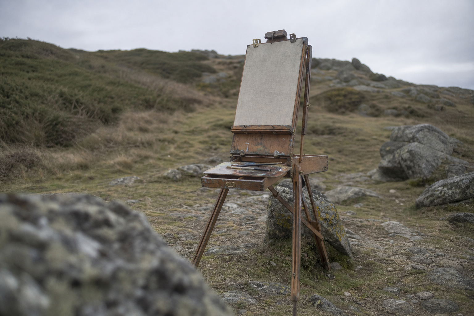 A traditional wooden French box easel standing on rocky uneven terrain outdoors
