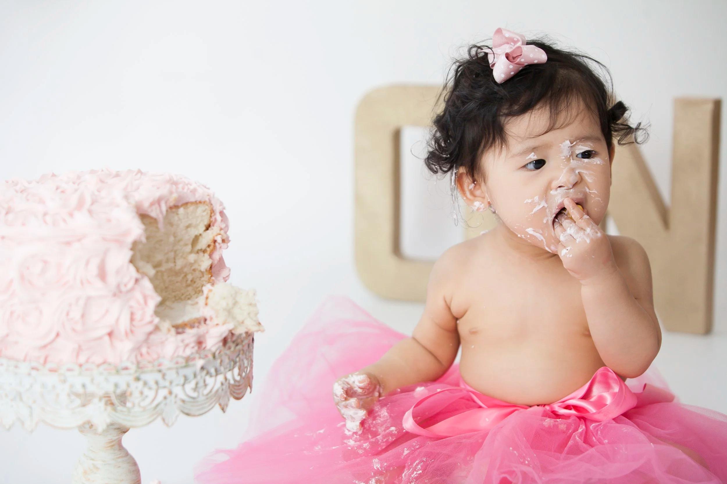 Baby girl in turquoise tutu and white One onesie tasting white rosette cake