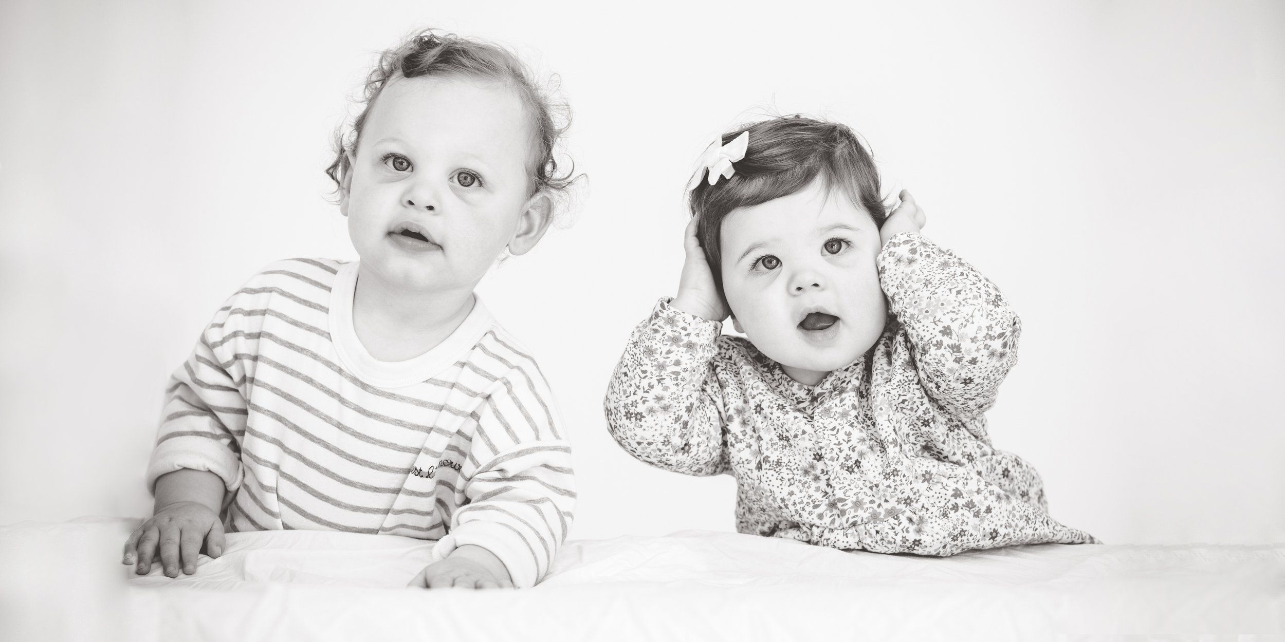Two toddler twin girls sitting together in cream dresses
