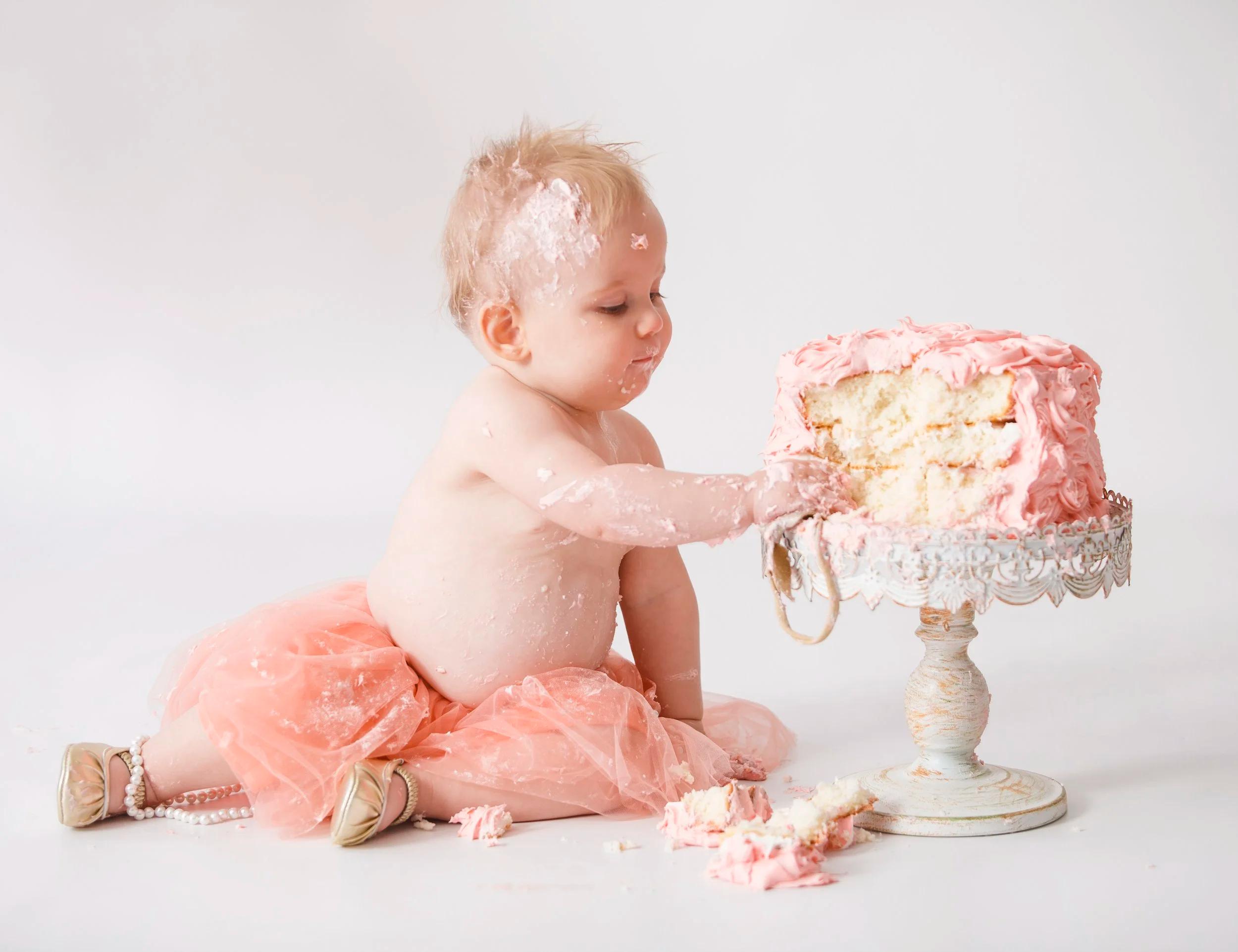 Baby boy touching finger to lip with cake in background