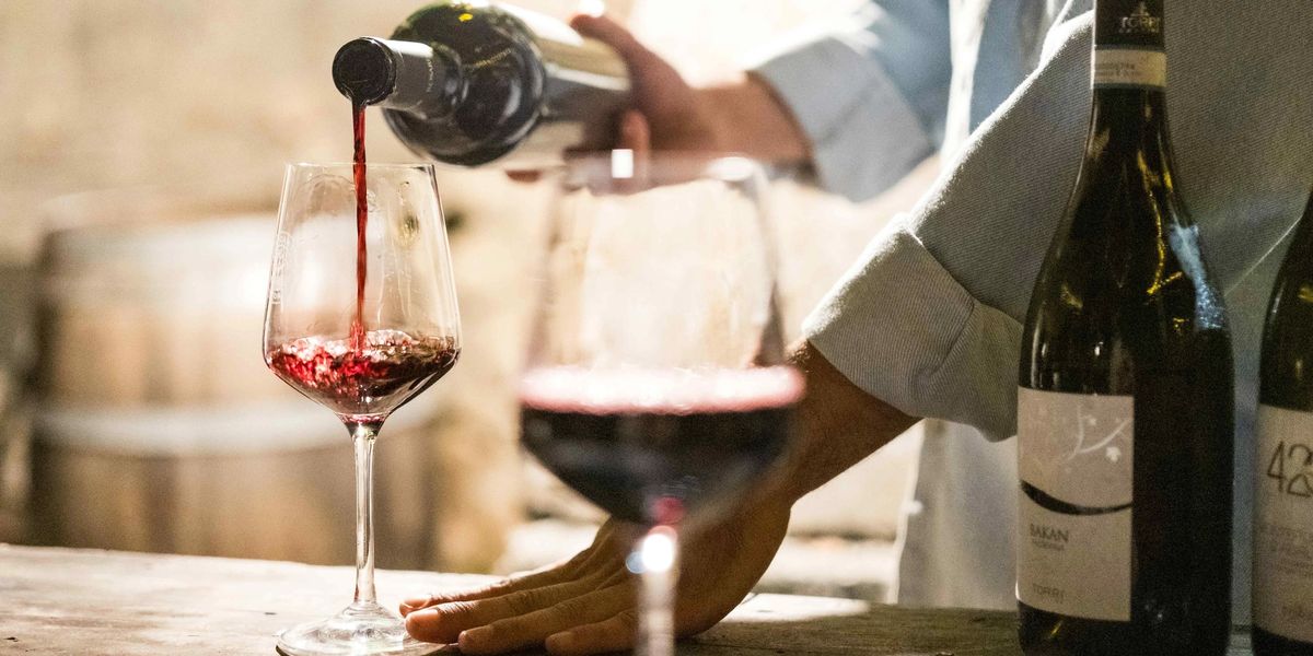 Red wine being poured into a wine glass on a wooden table.
