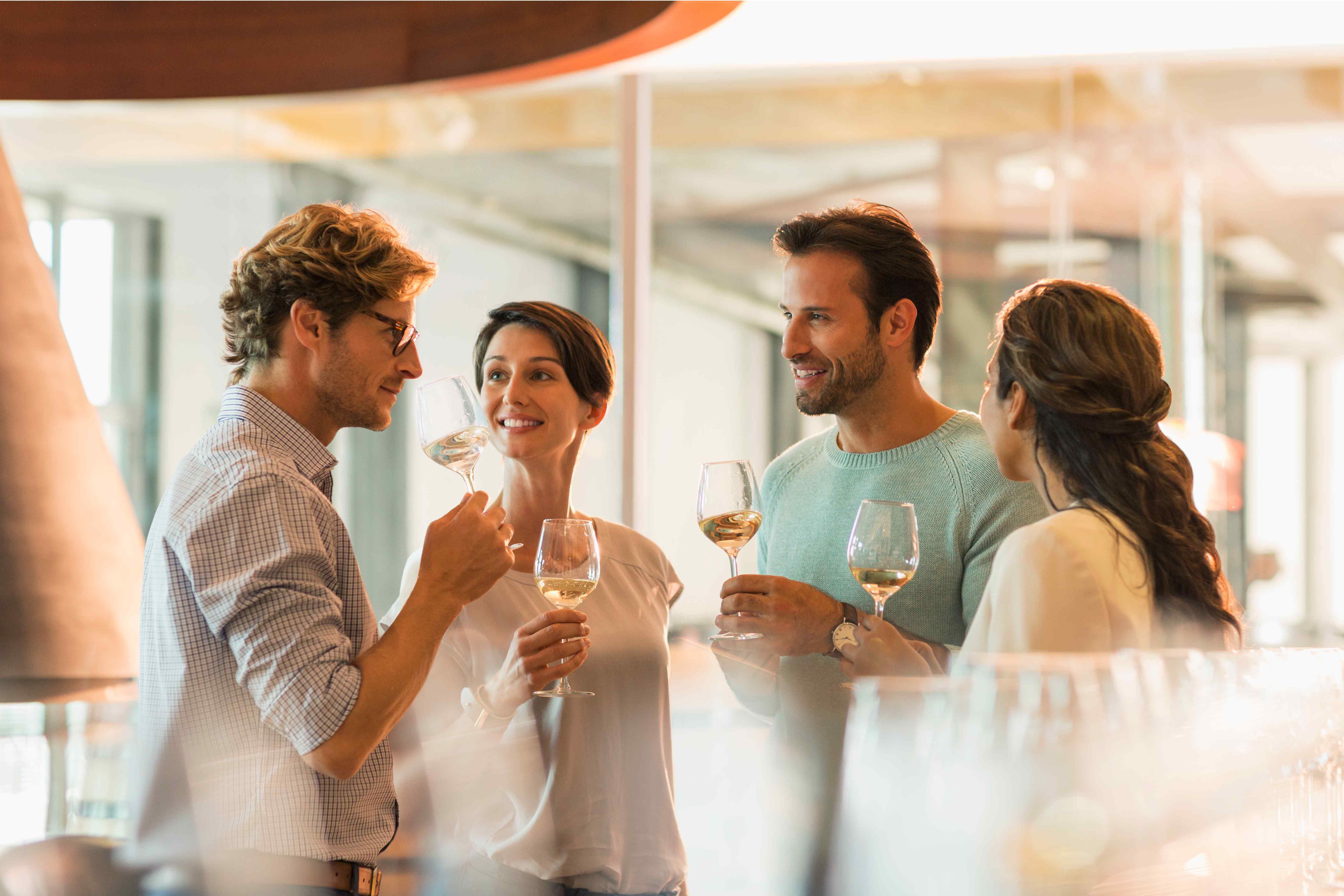 A group of smiling people standing and sipping from wine glasses, enjoying a bottle of white wine together.